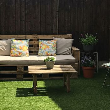 Un ejemplo de idea inspirado para decorar tu patio con: varias macetas con flores, mesas de madera, sillas de madera y un sofa de madera con cojines para estar cómodo.
