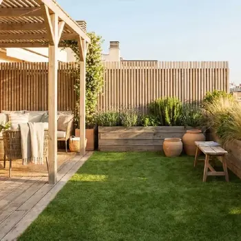 Sun-drenched rooftop terrace featuring a wooden pergola over a cozy lounge area, a green lawn, and raised wooden planters filled with lavender and greenery, creating a serene urban oasis against a city skyline.