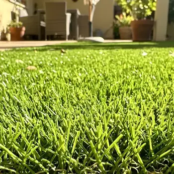 Primer plano de fibras de césped artificial Turfgrass en un jardín, mostrando su textura realista y color verde vibrante bajo la luz del sol.