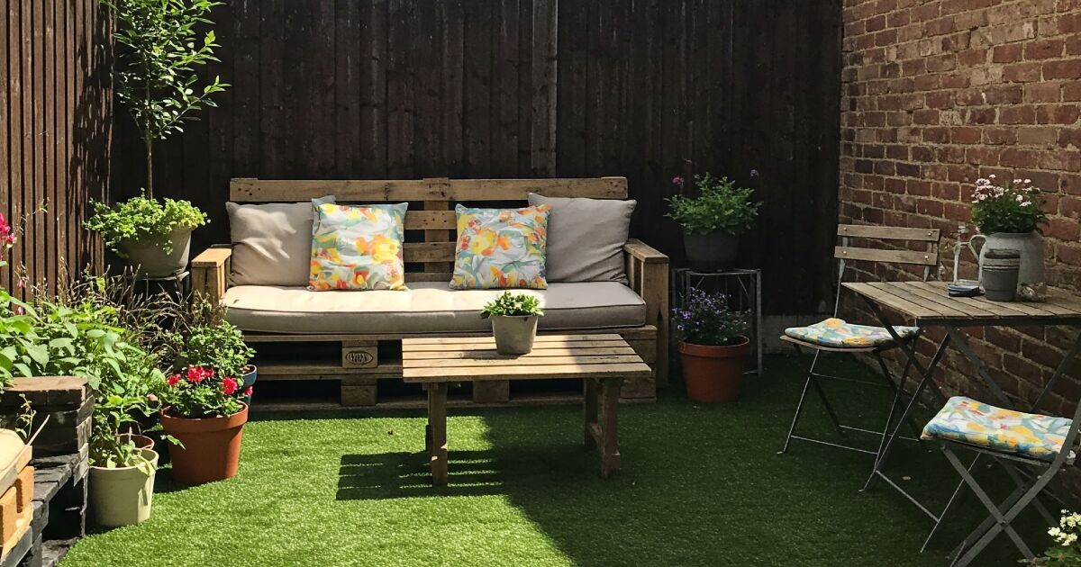 Un ejemplo de idea inspirado para decorar tu patio con: varias macetas con flores, mesas de madera, sillas de madera y un sofa de madera con cojines para estar cómodo.