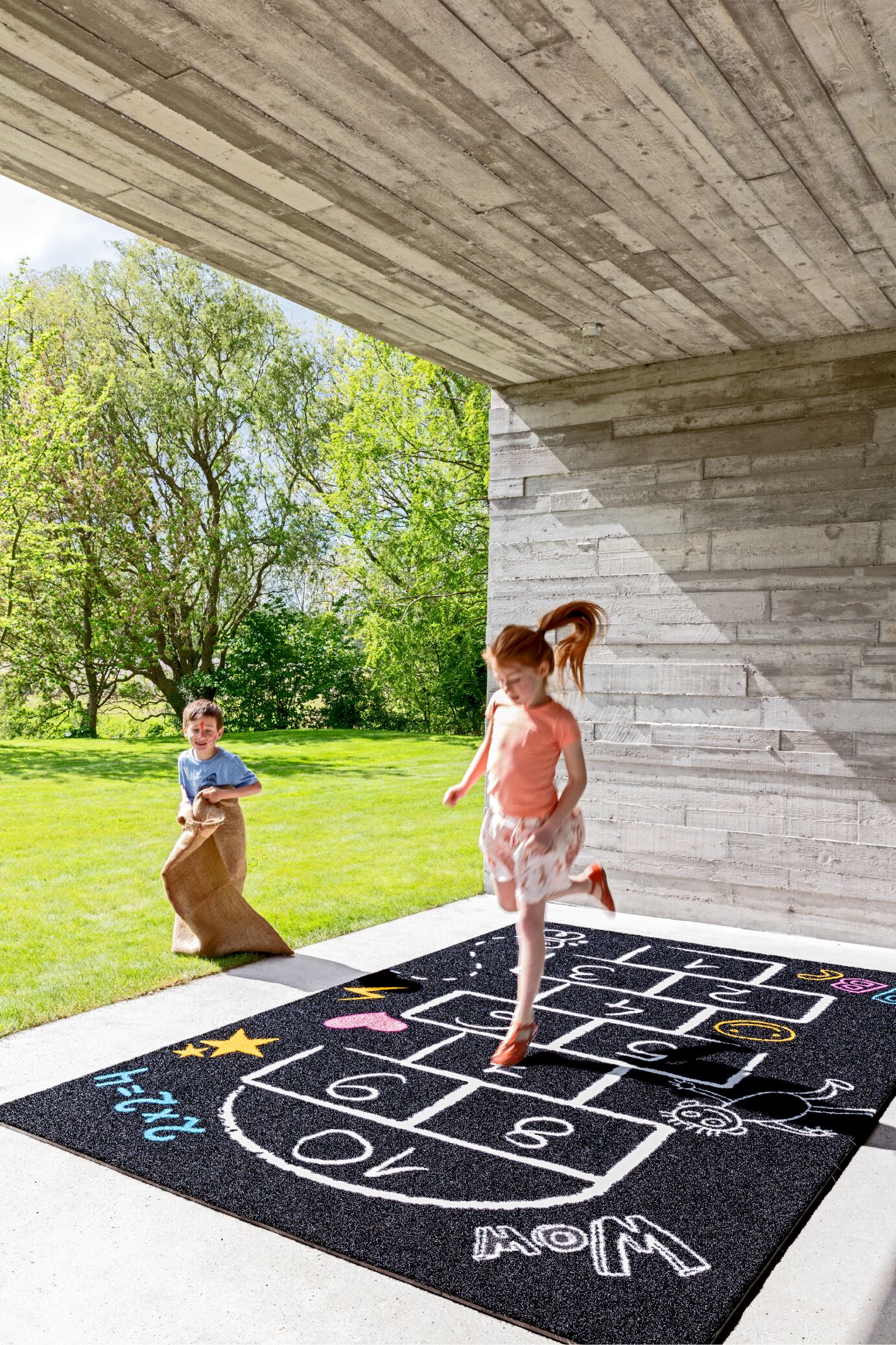 Niños jugando sobre una rayuela dibujada en el suelo tras instalar césped artificial en zonas infantiles.