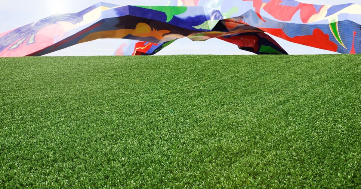 Imagen en la que se ve un césped artificial con una pared que ha sido pintada con varios colores y han hecho unos diseños.