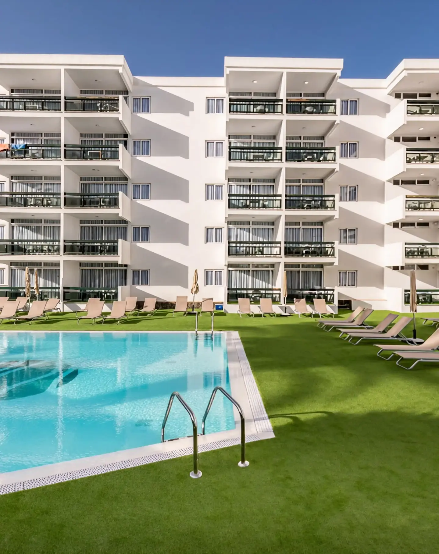 Outdoor area of hotel with swimming pool and sun loungers after the installation of Turfgrass artificial turf for hospitality.