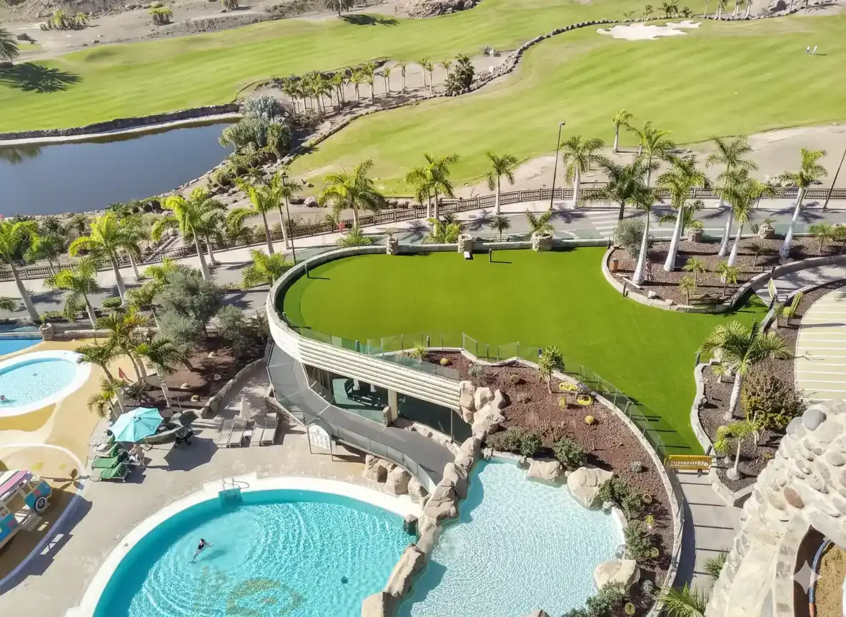 Aerial view of hotel and golf course showing an infinity pool and communal area with synthetic grass for businesses.