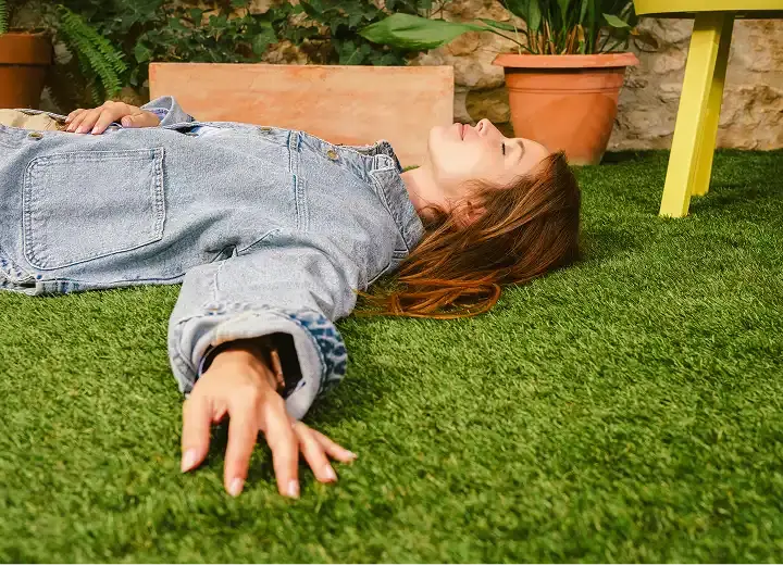 Woman resting on indoor artificial grass with one arm stretched out on the grass.