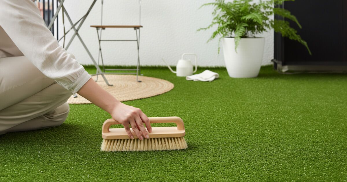 Frau, die sich auf einem kleinen Balkon oder einer Terrasse um Kunstrasen kümmert.