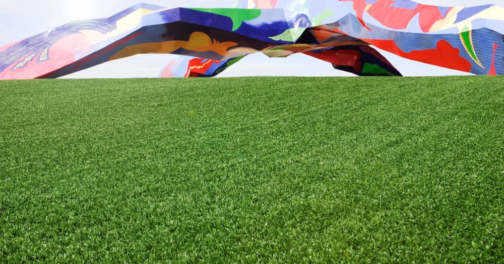 Imagen en la que se ve un césped artificial con una pared que ha sido pintada con varios colores y han hecho unos diseños.